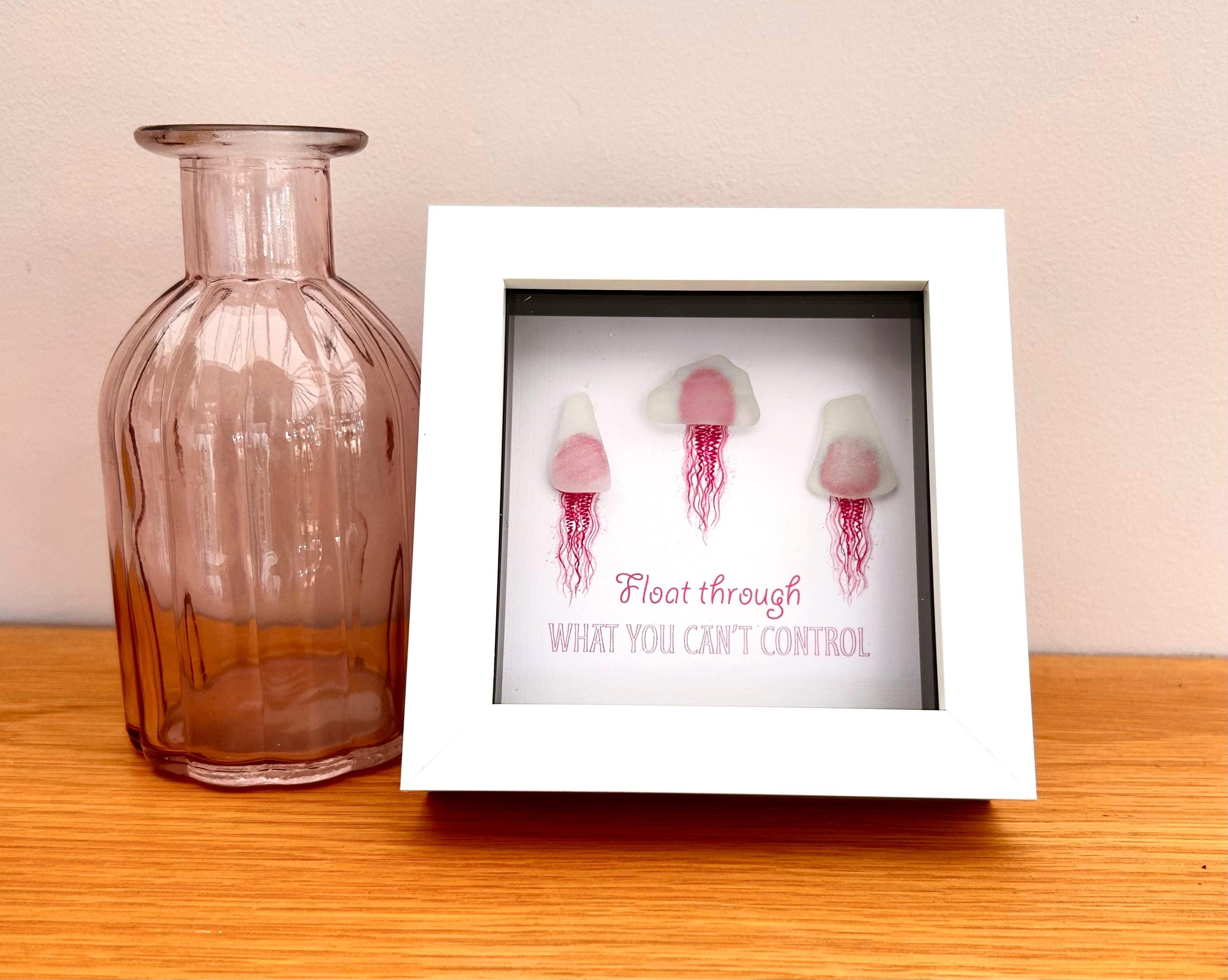 Pink sea glass jellyfish art in white frame with calming coastal quote wall decor in a home setting