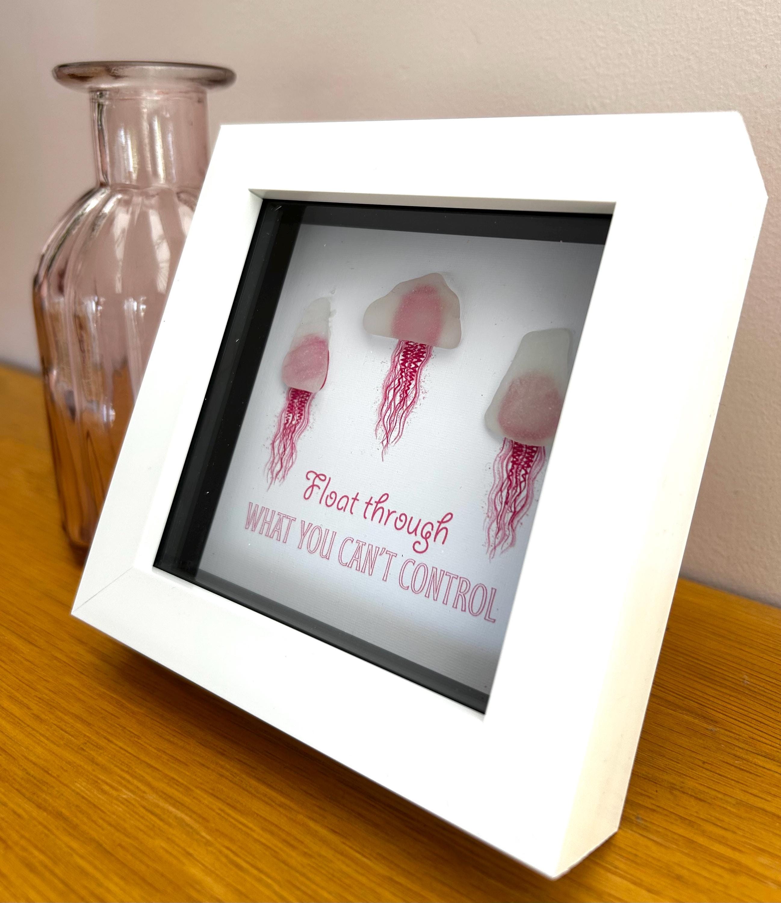 Pink sea glass jellyfish art in white frame with calming coastal quote wall decor in a home setting